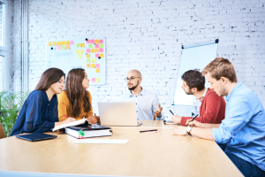 Five colleagues discussing around a table in a brick-walled meeting room